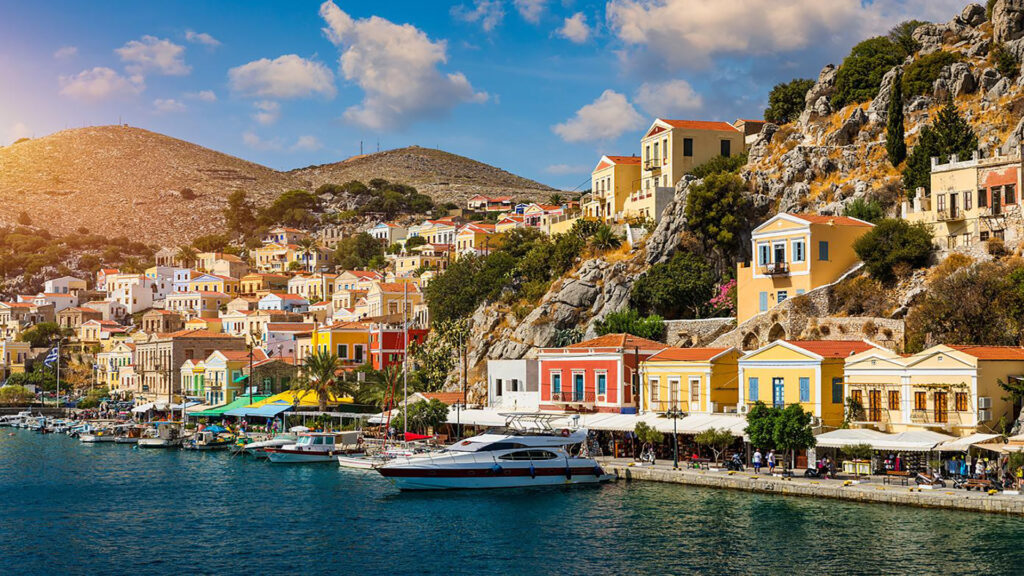 Symi's waterfront, with pastel neoclassical houses and a yacht moored alongside