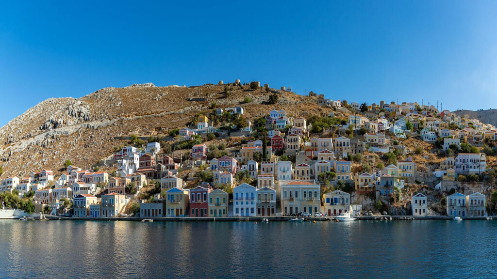 Panoramic view of Symi's pastel houses rising up the hillside above the harbour