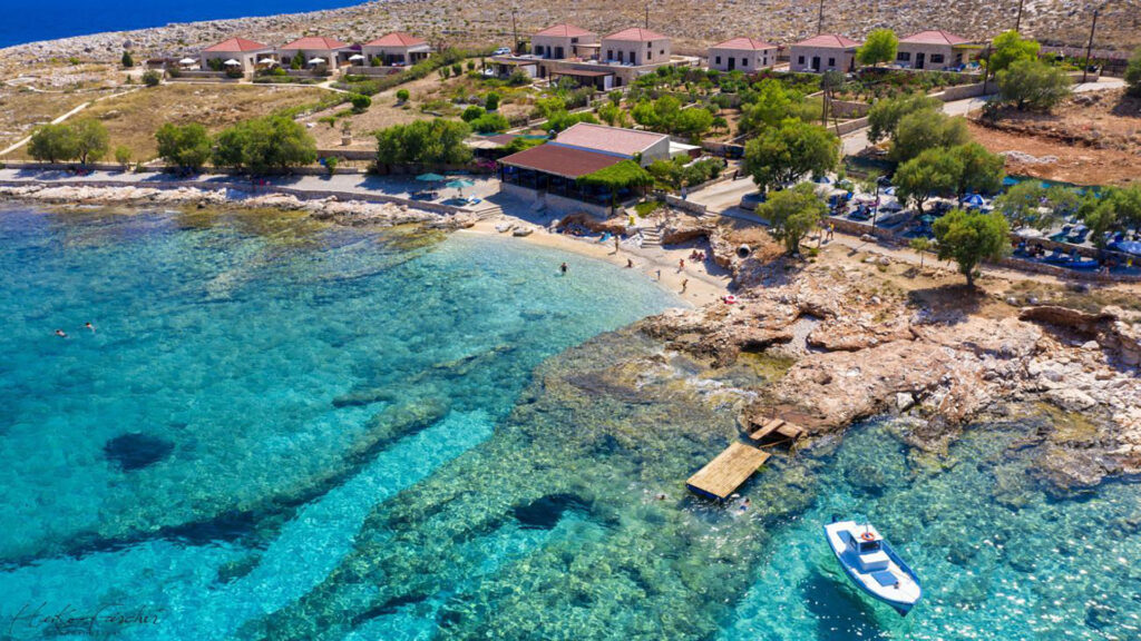 Aerial view of Ftenagia Beach on Chalki, with stone villas and swimmers in the clear turquoise water
