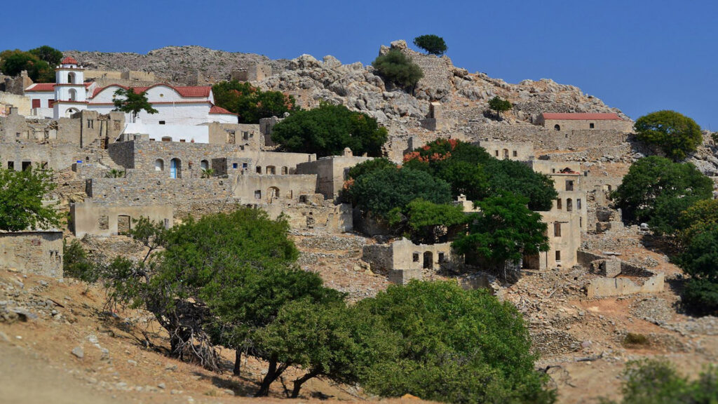 View of Mikro Chorio, an abandoned stone village on a hillside with a whitewashed church