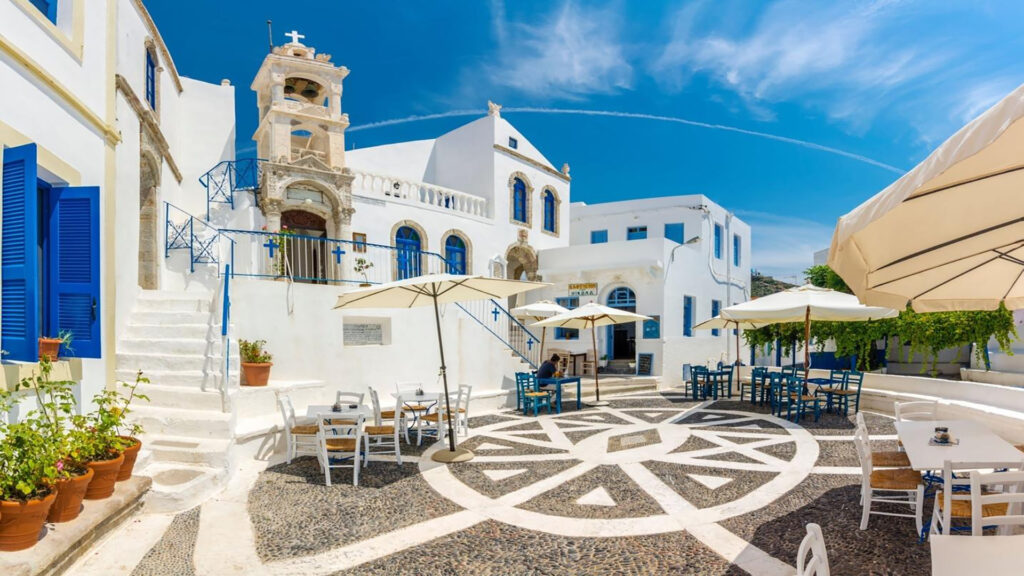 View of a traditional square in Nisyros, with a whitewashed church, mosaic-paved courtyard and café tables