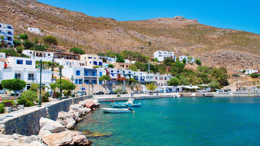 View of Tilos harbor, with whitewashed buildings lining the waterfront and boats moored below