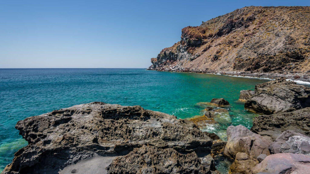 View of Volcanis Beach on Nisyros, with turquoise water framed by dark volcanic cliffs